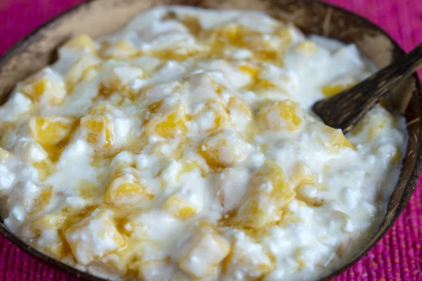 Slices of ripe sweet yellow mango fruit with white cottage cheese, honey and sour cream in coconut bowl , closeup — Stock Photo, Image