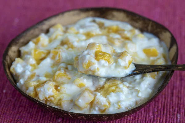 Slices of ripe sweet yellow mango fruit with white cottage cheese, honey and sour cream in coconut bowl , closeup — Stock Photo, Image