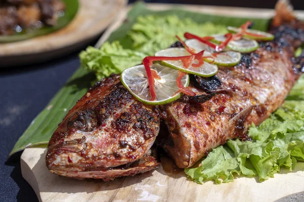 Smažená ryba s čerstvým zeleným salátem a citronem z Bali, Indonésie, uzavřena. Lahodné pečené mořské ryby s citronem na dřevěné desce v restauraci — Stock fotografie