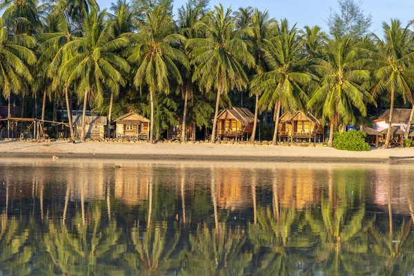 Залив с кокосовыми пальмами и деревянными балаганами, который отражается в морской воде. Пляж с песком, зеленые пальмовые листья и морская вода на острове Пханган, Таиланд — стоковое фото