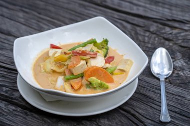 Krem kırmızı karışık sebzeler bir ahşap masa üzerinde beyaz bir plaka tofu ile Hindistan cevizi sosu köri, geleneksel Tay gıda.