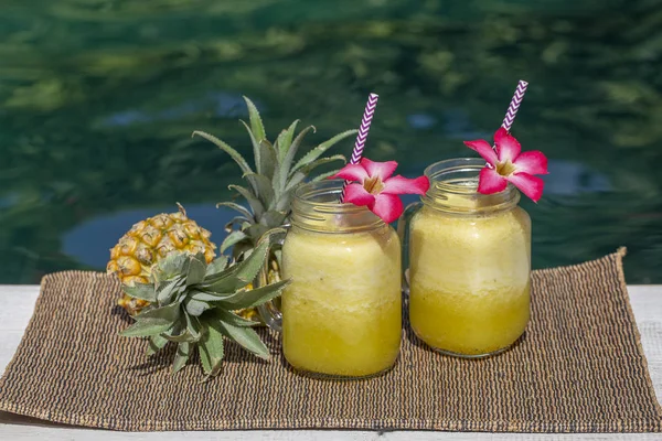 Batido casero de mango y piña hecho con leche de coco en dos jarras de vidrio cerca de la piscina. Isla Bali, Indonesia. Refrescante bebida de frutas tropicales —  Fotos de Stock