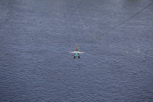 Οπίσθια όψη του νεαρού άνδρα ιππασία σε zip line σε φόντο ενός κυανού κύματος του ποταμού, Κίεβο, Ουκρανός — Φωτογραφία Αρχείου