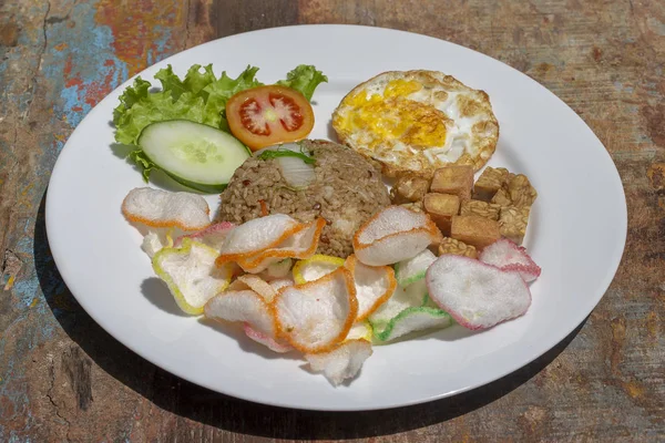 Stekt ris med grönsaker, ris chips, ost tofu och stekt ägg på det gamla träbordet i det lokala kaféet, närbild indonesiska köket. Frukost på Bali, Indonesia — Stockfoto