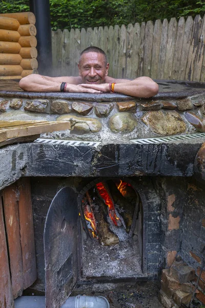 Happy Man kąpieli w żeliwnym VAT z wodą mineralną zawierającą siarkowodoru. Woda w żeliwnych VATS podgrzewana do 40-45 stopni Celsjusza. Ukraina, region karpacki — Zdjęcie stockowe