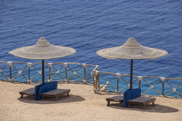 Two straw umbrellas with wooden sun loungers next to the red sea on sand beach at the resort in Sharm El Sheikh, Egypt — Stock Photo, Image