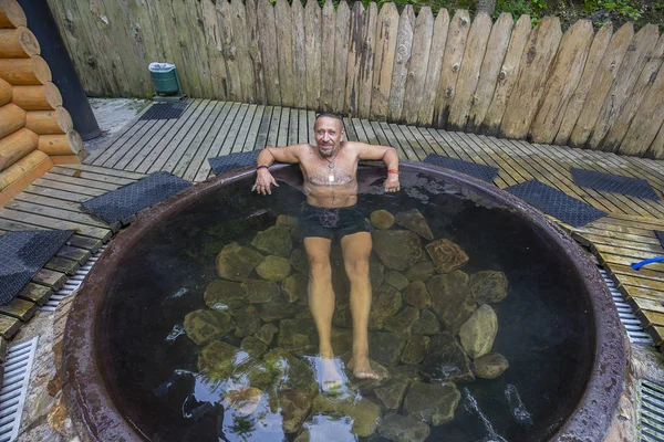 Happy Man kąpieli w żeliwnym VAT z wodą mineralną zawierającą siarkowodoru. Woda w żeliwnych VATS podgrzewana do 40-45 stopni Celsjusza. Ukraina, region karpacki — Zdjęcie stockowe