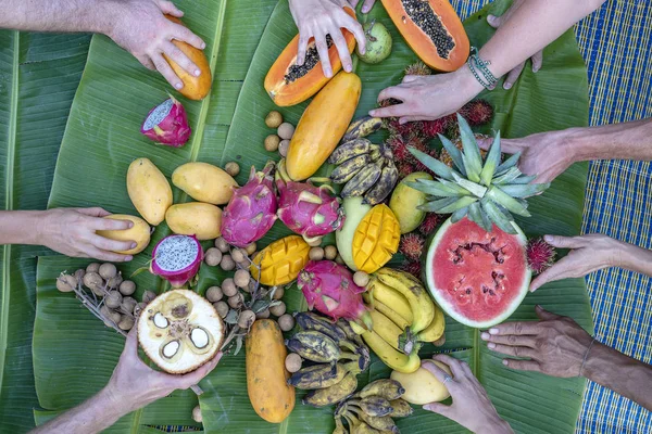 Tropiska frukter sortiment på en grön bananblad och människor händer. Smaskiga dessert, närbild. Mango, papaya, pitahaya och händer, uppifrån — Stockfoto