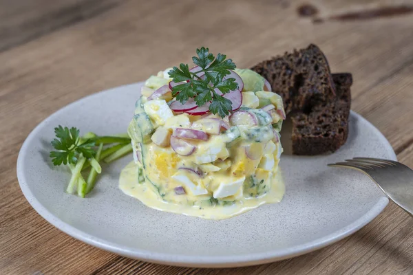Вкусный салат с огурцом, редиской и яйцом со сливочным соусом в тарелке на деревянном фоне. Здоровое питание, крупный план — стоковое фото