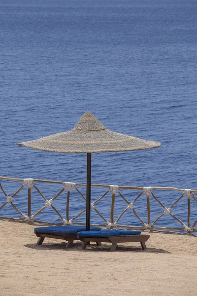 Straw umbrellas with wooden sun loungers next to the red sea on sand beach at the resort in Sharm El Sheikh, Egypt — Stock Photo, Image
