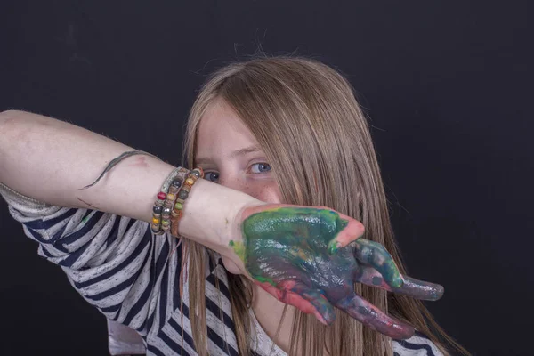 Bela menina loira com sardas e mãos pintadas em tintas coloridas dentro de casa em fundo preto, close up retrato — Fotografia de Stock