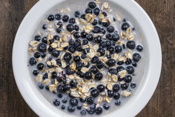신선한 블루베리, 아몬드 밀크, 꿀을 곁들인 오트밀은 나무 배경의 접시에 담았습니다. 소박한 스타일. 맨 위 보기. — 스톡 사진