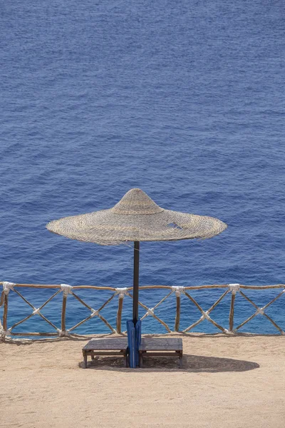 Sombrillas de paja con tumbonas de madera junto al mar rojo en la playa de arena en el complejo en Sharm El Sheikh, Egipto — Foto de Stock