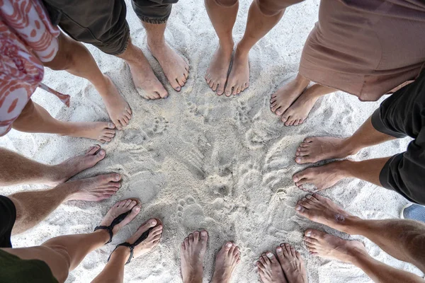 Muchas piernas femeninas y masculinas están de pie juntos en la arena cerca del mar, concepto de vacaciones de verano. Vista superior — Foto de Stock