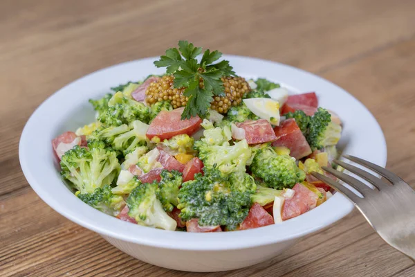 Lahodný salát s brokolicí, rajčaty, cibulí a vařenými vejci se smetanovou omáčkou na dřevěném podkladu. Zdravé jídlo — Stock fotografie