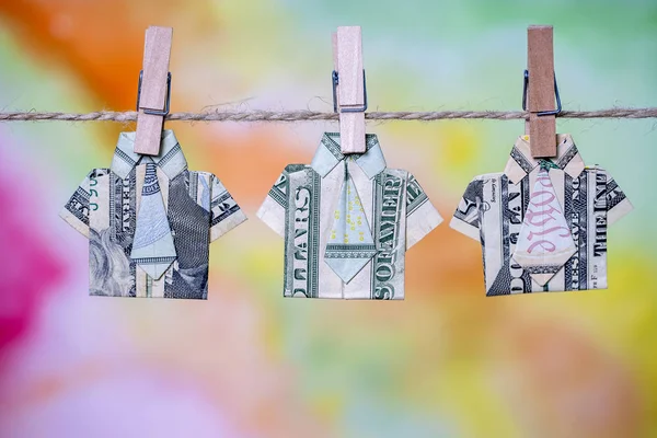 Camisa de origami hecha de billete de dólar sobre fondo colgante de colores. Billetes de un dólar colgados de una cuerda. De cerca. —  Fotos de Stock