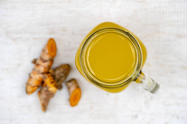 Energy tonic drink with turmeric, ginger, lemon and honey in glass mug, white wooden background, close up, top view