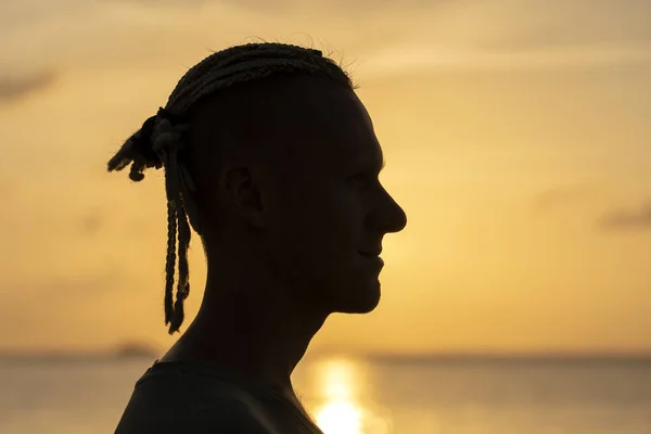 Silhueta de um jovem com dreadlocks na cabeça perto do mar durante o pôr do sol. Fechar retrato — Fotografia de Stock