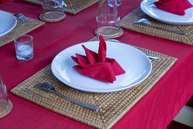 Restoranda çatal, kaşık, beyaz plaka ve kırmızı peçete ile zarif masa ayarı. Düzenlenmiş gümüş ve peçeteler ile güzel yemek masası seti