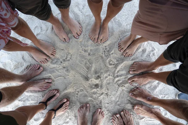 Muchas piernas femeninas y masculinas están de pie juntos en la arena cerca del mar, concepto de vacaciones de verano. Vista superior — Foto de Stock