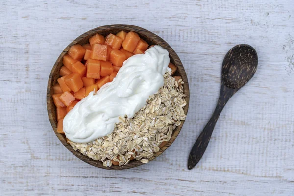 Scheiben süße Papaya mit Haferflocken und weißem Joghurt in Kokosnussschale auf weißem Holzhintergrund, Nahaufnahme — Stockfoto