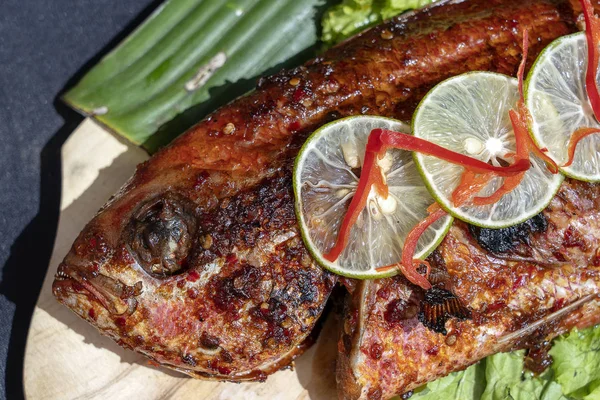 Gebakken vis met verse groene salade en citroen van Bali, Indonesië, close-up. Heerlijke geroosterde zeevis met citroen op houten bord in restaurant — Stockfoto