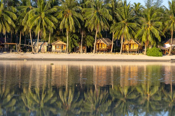 Vacker vik med kokospalmer och träbungalower som återspeglas i havsvatten. Tropisk sandstrand, grönt palmblad och havsvatten på ön Koh Phangan, Thailand — Stockfoto