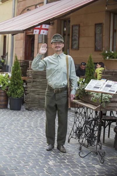 Ukrainischer Mann in der Uniform der ukrainischen Aufständischen Armee mit einem Gewehr lädt Touristen ein, das Restaurant auf der Straße im Stadtzentrum von Lwiw, Ukraine zu betreten — Stockfoto