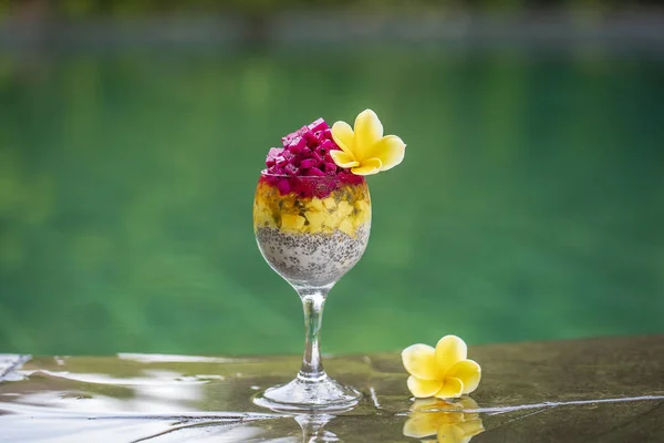 Pouding aux graines de chia avec fruits du dragon rouge, fruit de la passion, mangue et avocat dans un verre pour le petit déjeuner sur le fond de l'eau de la piscine, gros plan. Le concept de saine alimentation . — Photo