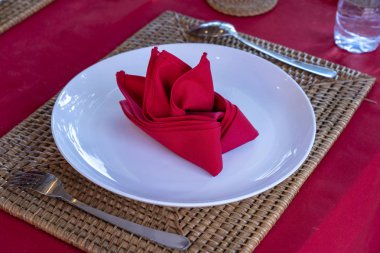 Restoranda çatal, kaşık, beyaz plaka ve kırmızı peçete ile zarif masa ayarı. Düzenlenmiş gümüş ve peçeteler ile güzel yemek masası seti