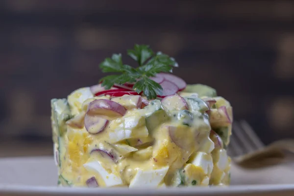 Delicious saláta uborka, retek és tojás tejszínes mártással egy tányéron fából készült háttérrel. Egészséges étkezés, közelről — Stock Fotó