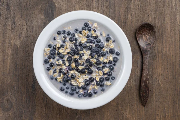 Harina de avena con arándanos frescos, leche de almendras y miel para el desayuno en plato sobre fondo de madera. Estilo rústico. Vista superior . — Foto de Stock