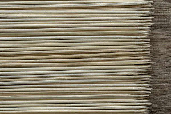 Mucchio di bastoncini di legno o spiedini di bambù utilizzati per tenere insieme pezzi di cibo su sfondo di legno — Foto Stock
