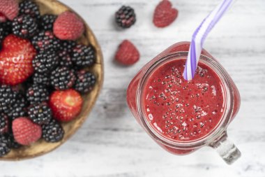 Beyaz masa üzerinde cam kupa taze organik kırmızı smoothie, yakın, üst görünümü. Ferahlatıcı yaz meyve içeceği. Böğürtlen, ahududu ve çilek yüzlü