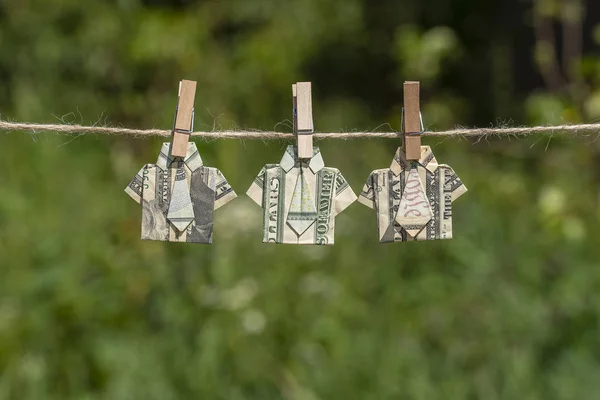Camisa de origami hecha de billete de dólar sobre fondo verde de la naturaleza. Billetes de un dólar colgados de una cuerda. De cerca. —  Fotos de Stock