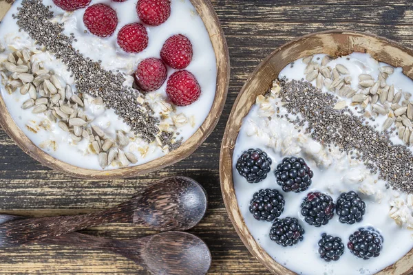 Smoothie dans un bol de noix de coco avec mûres, framboises, flocons d'avoine, graines de tournesol et graines de chia pour le petit déjeuner, fermer. Le concept d'une alimentation saine, superfood — Photo