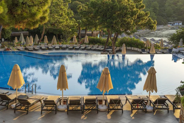 Camas de sol vazias e guarda-sóis fechados pela manhã, junto à piscina do hotel. Piscina em resort de hotel de luxo perto do mar. Linda paisagem marinha matinal. Turquia — Fotografia de Stock