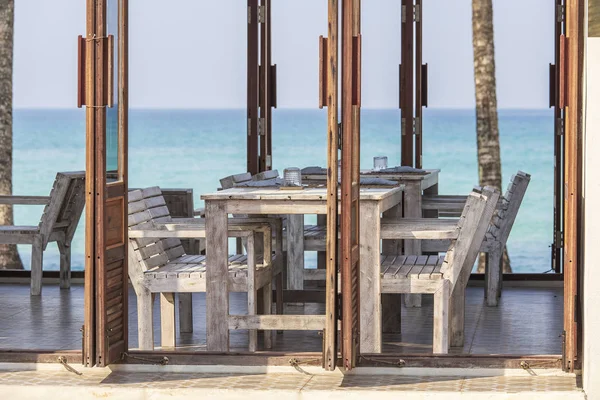 Tropisches Strandcafé mit Holztisch und Stühlen vor dem Hintergrund des blauen Meeres, Thailand. Reisekonzept — Stockfoto
