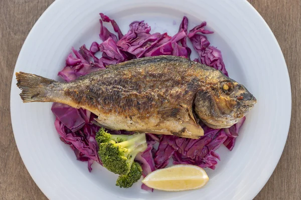 Peixes do mar grelhados servidos em um prato com repolho vermelho, brócolis verde e limão. Fechar — Fotografia de Stock