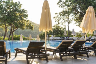 Sabahları otel havuzunun yanında boş şezlonglar ve kapalı şemsiyeler. Denize yakın lüks bir otel beldesinde yüzme havuzu. Güzel sabah deniz manzarası. Türkiye