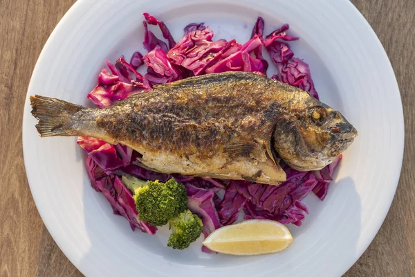 Grillowane ryby morskie podawane na talerzu z czerwoną kapustą, zielonymi brokułami i cytryną. Zbliżenie — Zdjęcie stockowe