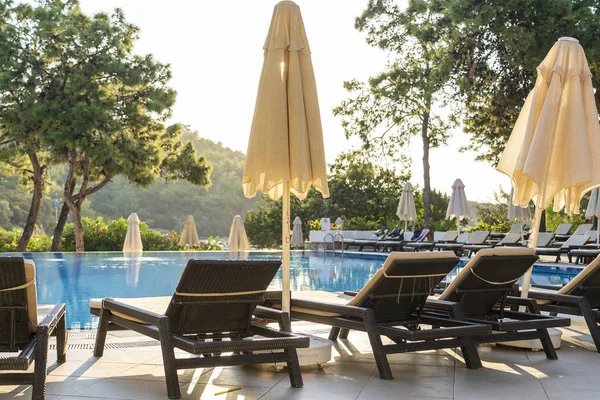 Camas de sol vazias e guarda-sóis fechados pela manhã, junto à piscina do hotel. Piscina em resort de hotel de luxo perto do mar. Linda paisagem marinha matinal. Turquia — Fotografia de Stock