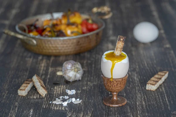 Мягкое вареное яйцо в яичной чашке с ломтиком поджаренного хлеба на фоне деревянного стола, крупным планом — стоковое фото