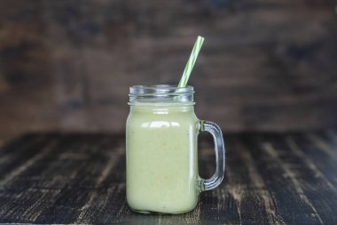 Avokado taze yeşil smoothie, muz ve bal ahşap arka plan üzerinde cam kupa, closeup. Sağlıklı beslenme kavramı