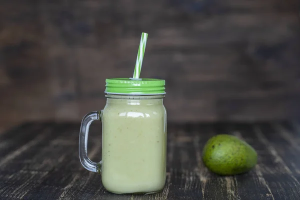Φρέσκο πράσινο χυμό από αβοκάντο, μπανάνα και μέλι σε γυάλινη κούπα σε ξύλινο φόντο, κοντινά πλάνα. Έννοια της υγιεινής διατροφής — Φωτογραφία Αρχείου