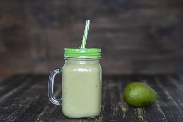 Batido verde fresco de aguacate, plátano y miel en taza de vidrio sobre fondo de madera, primer plano. Concepto de alimentación saludable — Foto de Stock