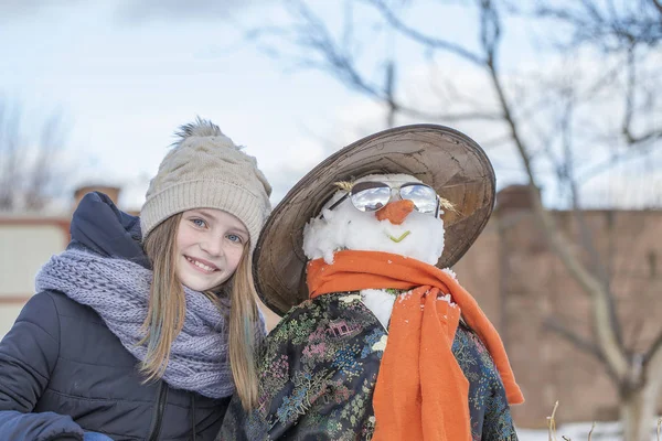 Rozkošná mladá dívka se sněžným mužem v krásném zimním parku. Zimní aktivity pro děti. Detailní — Stock fotografie