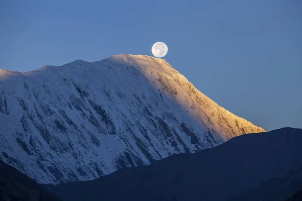 Bela paisagem no Himalaia, região de Annapurna, Nepal. Lua cheia durante um nascer do sol no fundo de montanhas cobertas de neve — Fotografia de Stock