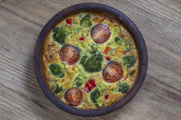 Ciotola in ceramica con frittata di verdure, semplice cibo vegetariano. Frittata con uova, pomodoro, pepe, cipolla, broccoli e formaggio sul tavolo di legno. frittata di uova italiane — Foto Stock