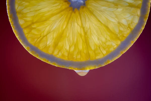 Rebanada de naranja fresca y gota de agua sobre fondo rojo, macro, primer plano — Foto de Stock